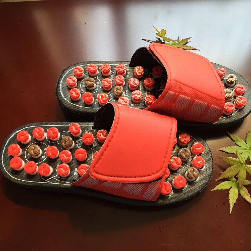 Red acupressure massage slippers with adjustable straps and raised massage nodes on brown surface