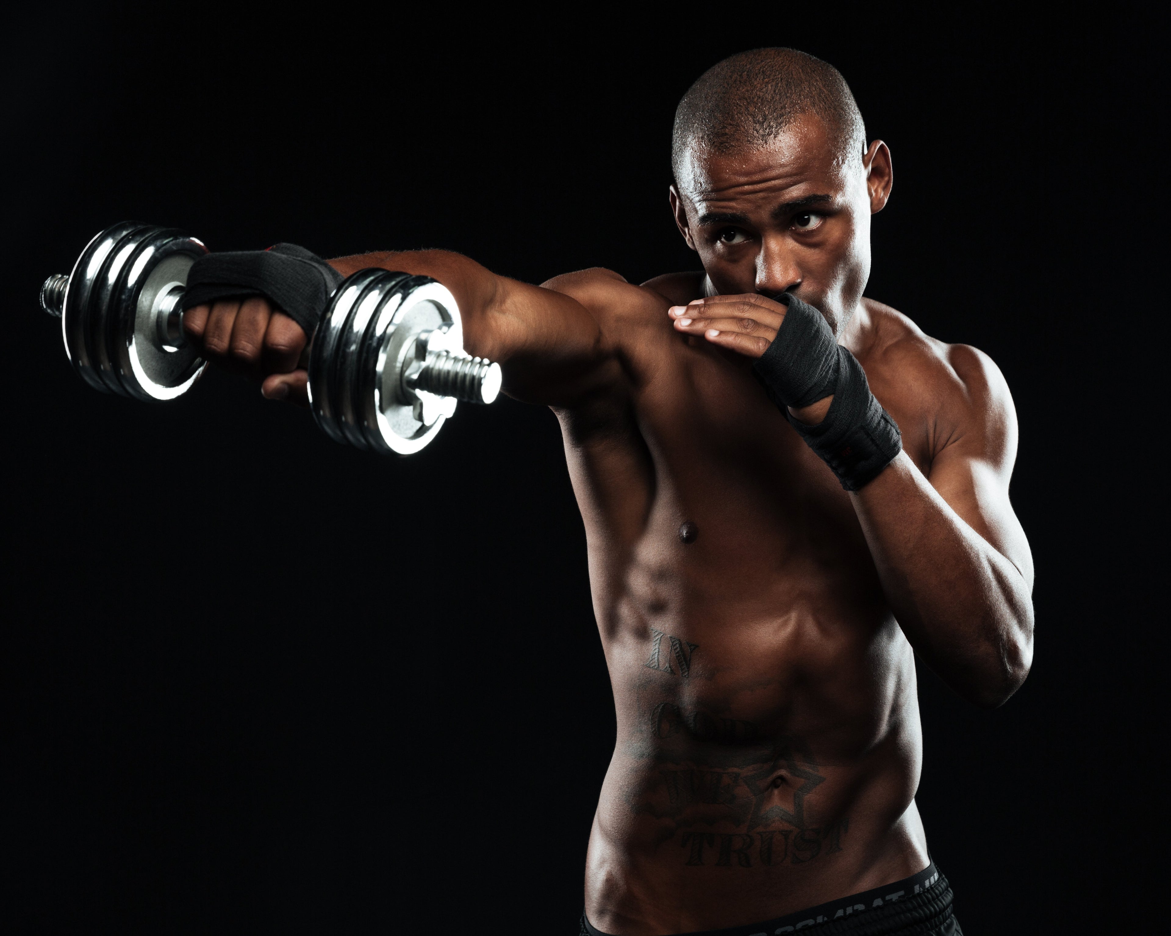 Fit man posing in fighting stance with dumbbells, promoting muscle recovery and strength training